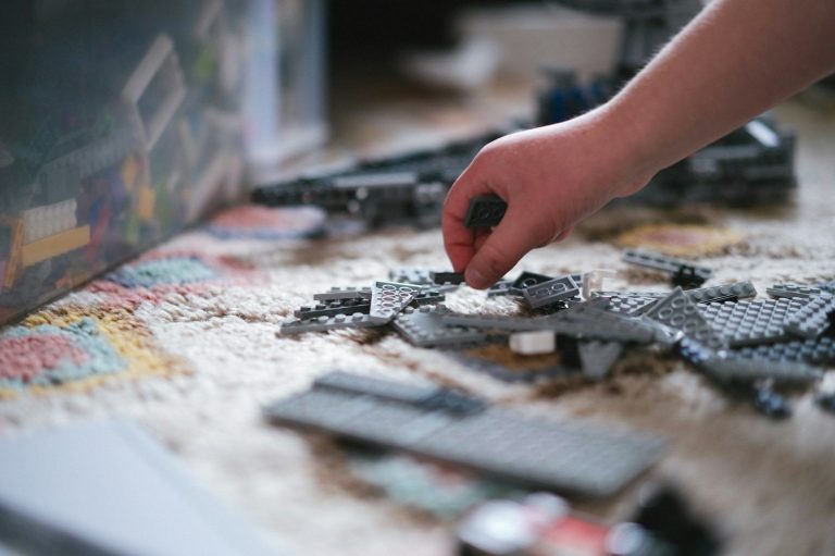 Eine Hand baut mit LEGO-Steinen auf einem Teppich.