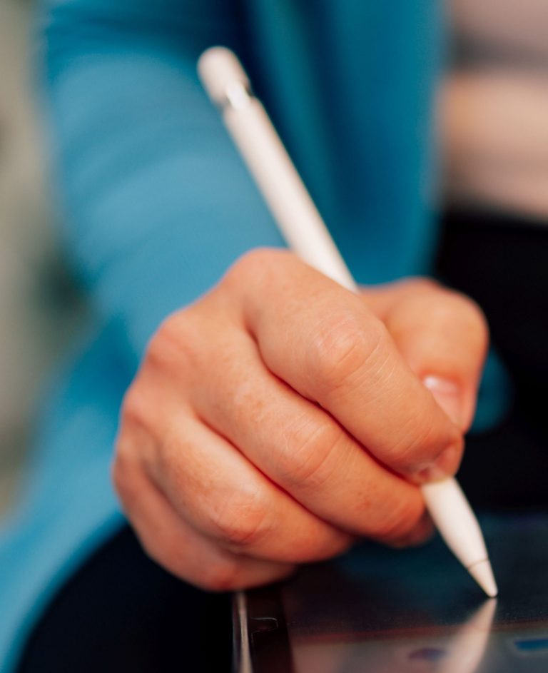 Eine Hand hält einen Stylus und schreibt auf einem Tablet.